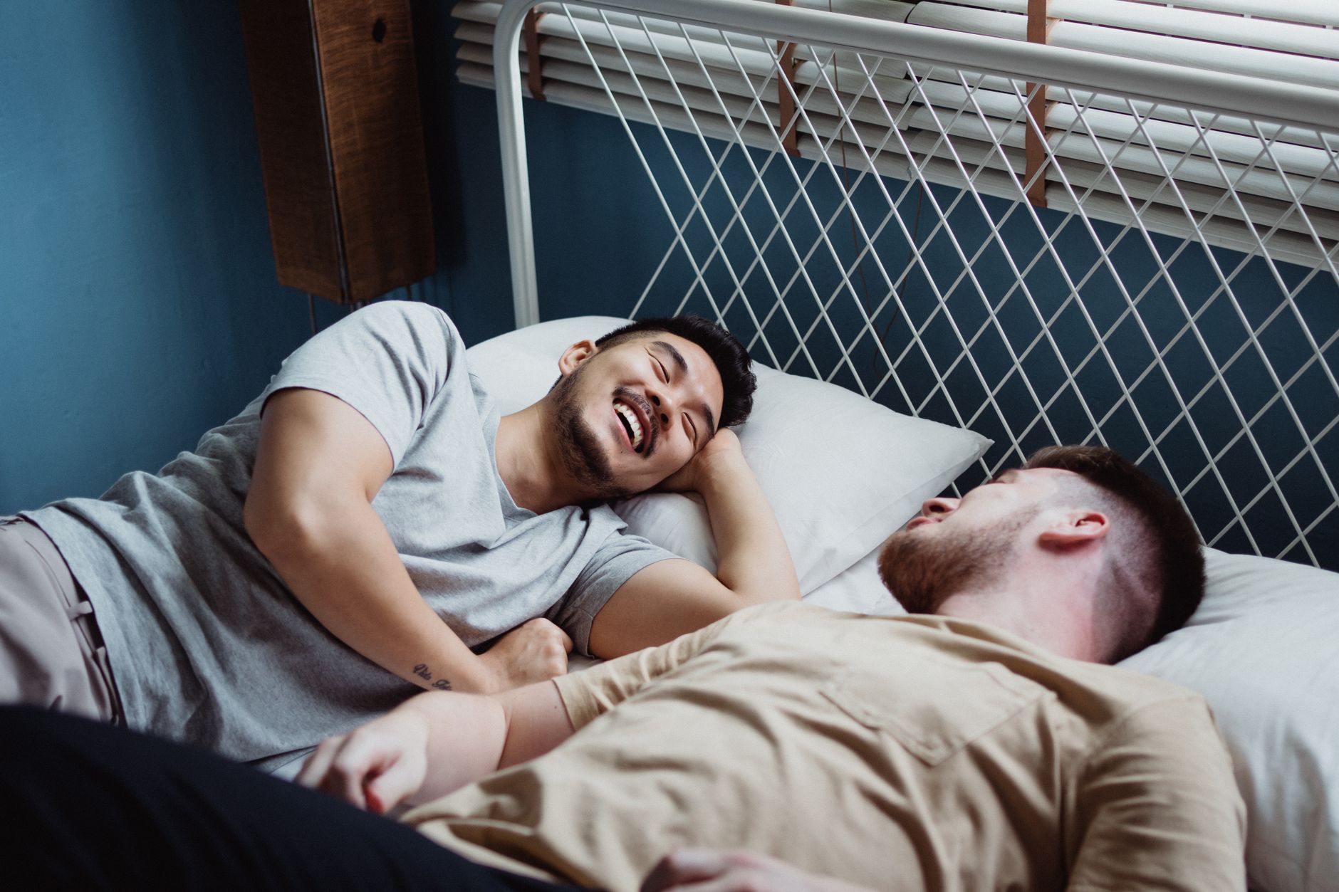 Two men laughing together in bed, comfortable and at ease