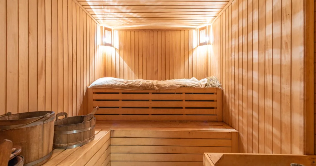 Warm amber-lit wooden sauna interior with empty benches, atmospheric editorial lighting